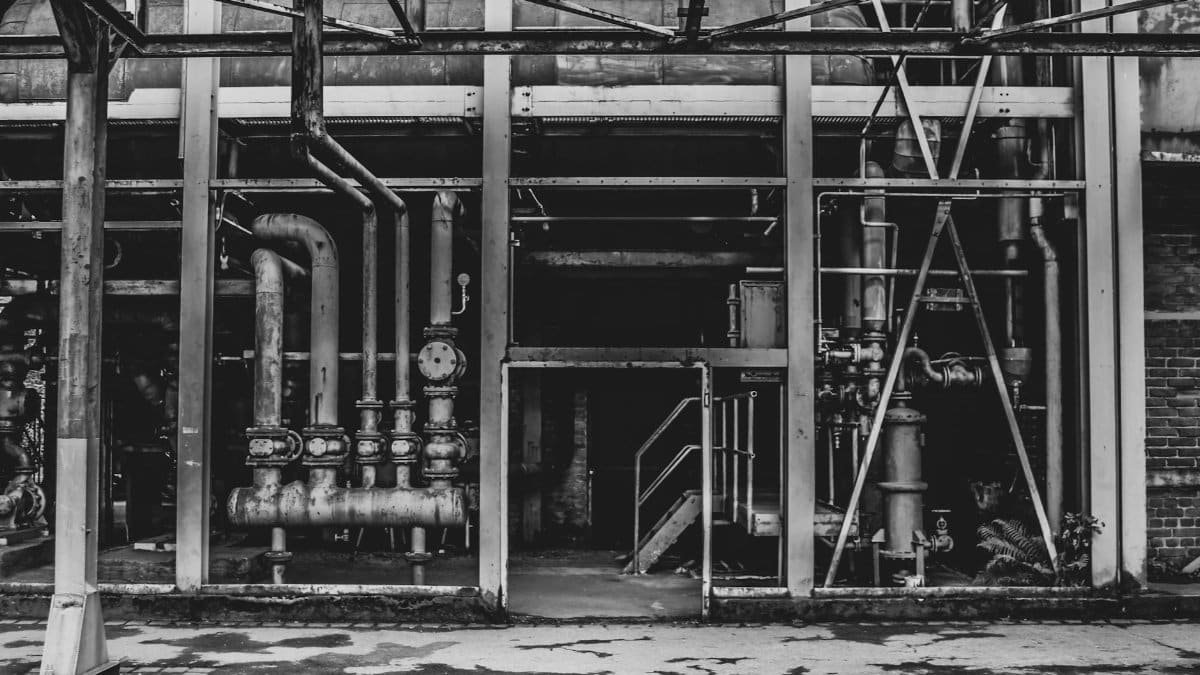 A black and white photo of an abandoned industrial building with exposed pipes and steel structures.