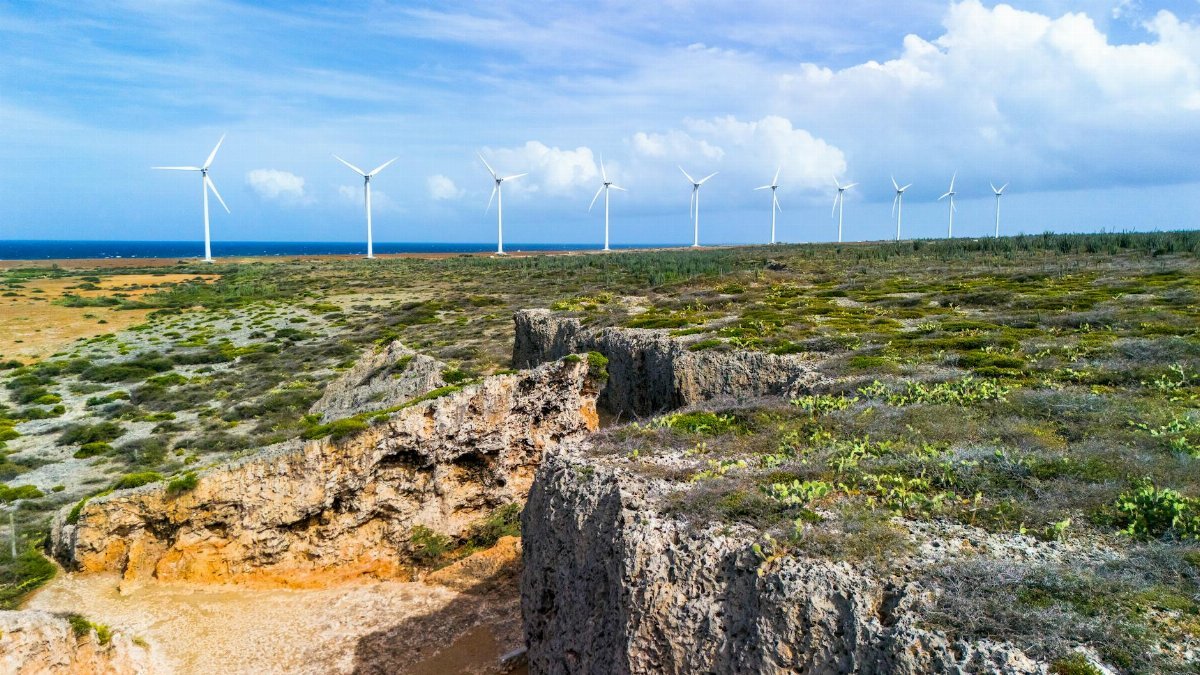 Aerial view of wind turbines along the rocky cliffs of a Caribbean coast with a clear blue sky and ocean.