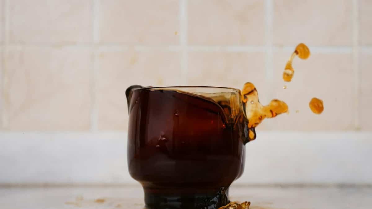 Brown glass cup with coffee splash against tiled background. Eye-catching spill captured mid-air.