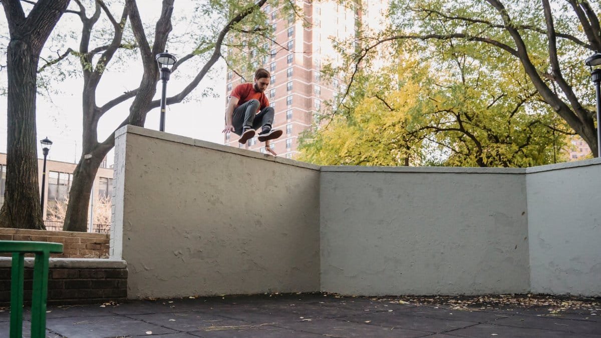 Agile male athlete jumping over obstacle while practicing parkour in town on summer day