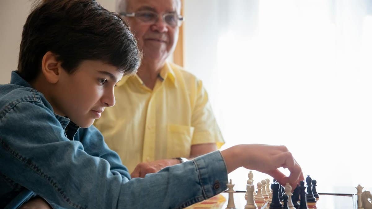A young boy and his grandfather playing chess indoors, captured with engaging expressions.