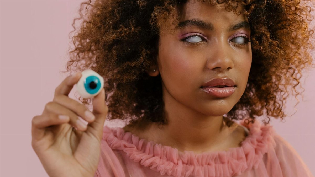 African American woman in pink with striking white eyes, holding a fake eyeball.