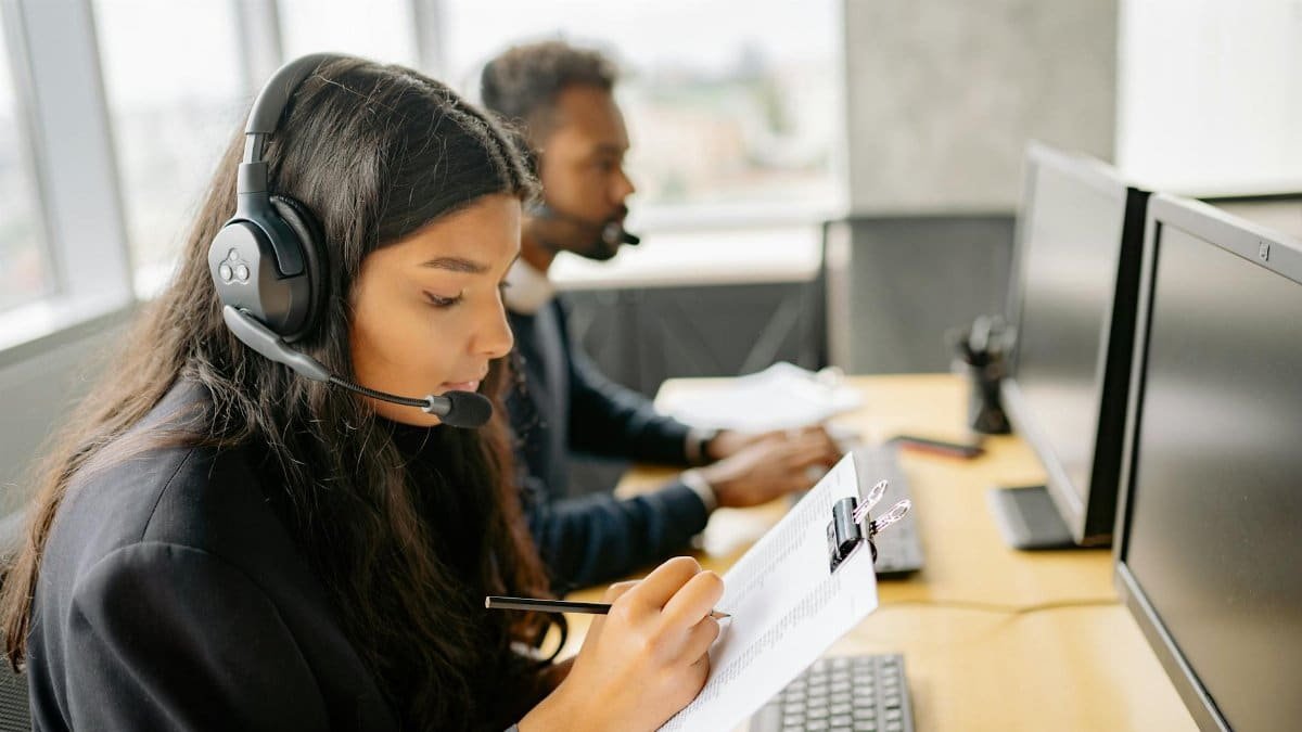 Two call center agents wearing headsets working at desks with computers in a modern office.