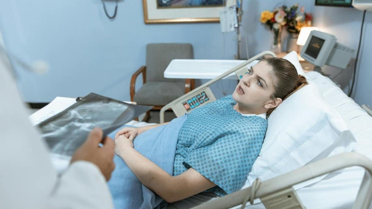 Caucasian woman in hospital bed receiving care from healthcare professional.