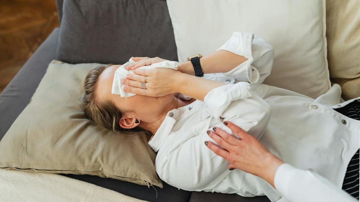 Woman lying on sofa being comforted with tissue during emotional moment indoors.