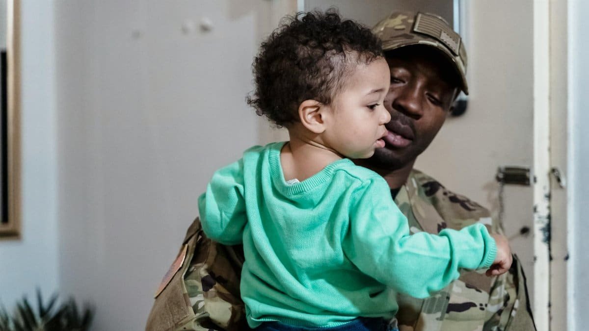 Military father in uniform lovingly holding his young child indoors.