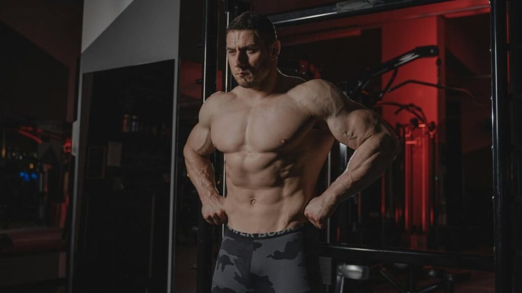 Shirtless bodybuilder flexing muscles under dramatic gym lighting. Fitness and strength.