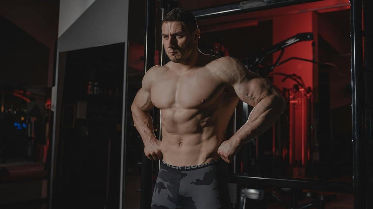 Shirtless bodybuilder flexing muscles under dramatic gym lighting. Fitness and strength.