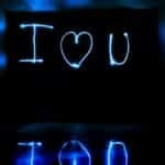 Blue neon light painting 'I love you' in a reflective dark tunnel.