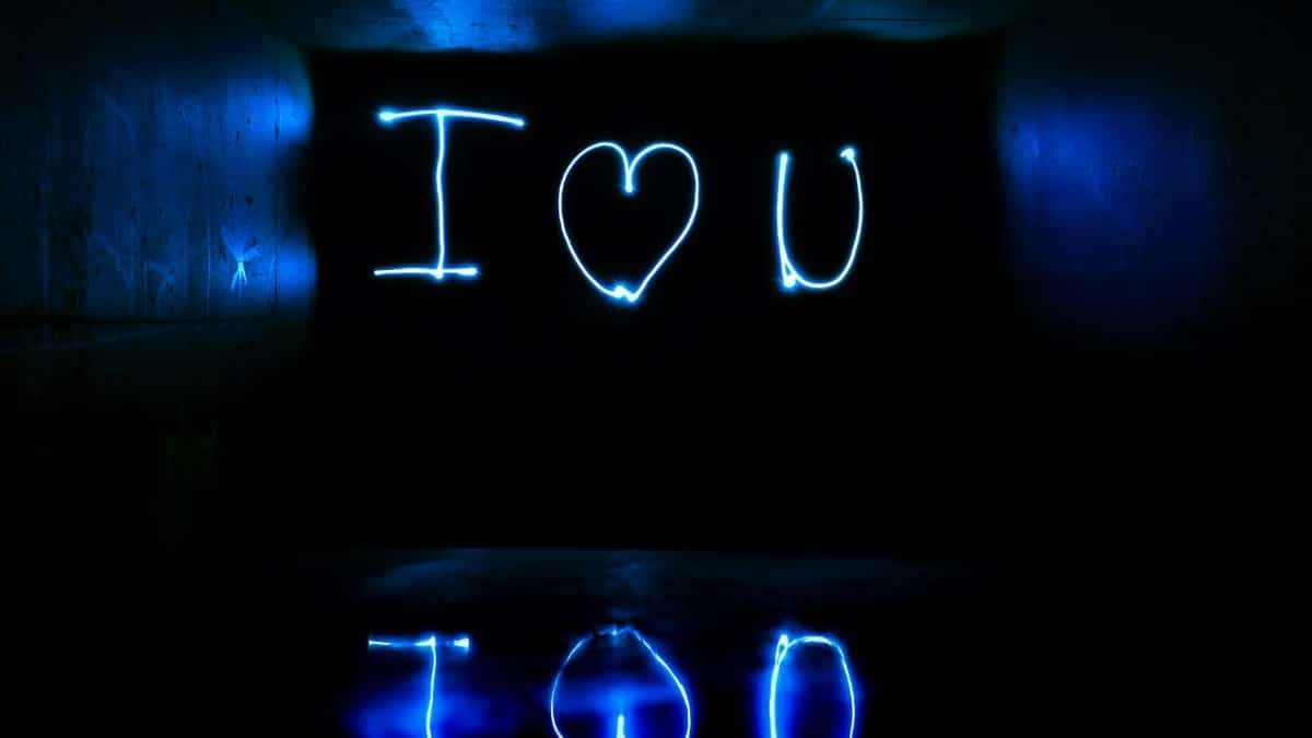 Blue neon light painting 'I love you' in a reflective dark tunnel.