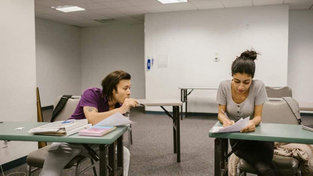 Two college students in a classroom setting, one appears to be copying from the other's paper.