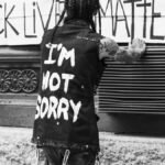 Back view of unrecognizable tattooed guy standing on street in front of banner with Black Lives Matter inscription
