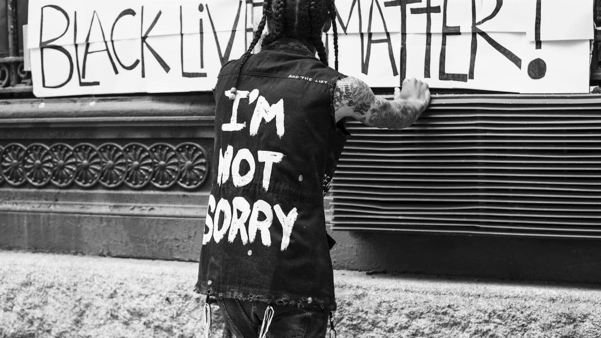 Back view of unrecognizable tattooed guy standing on street in front of banner with Black Lives Matter inscription