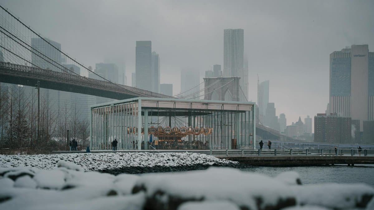 A winter scene featuring Jane's Carousel in Brooklyn with the iconic Brooklyn Bridge and New York skyline.