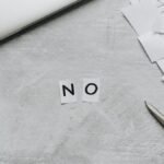 Top view of scattered paper squares, laptop, and scissors forming the word 'NO', implying rejection or denial.