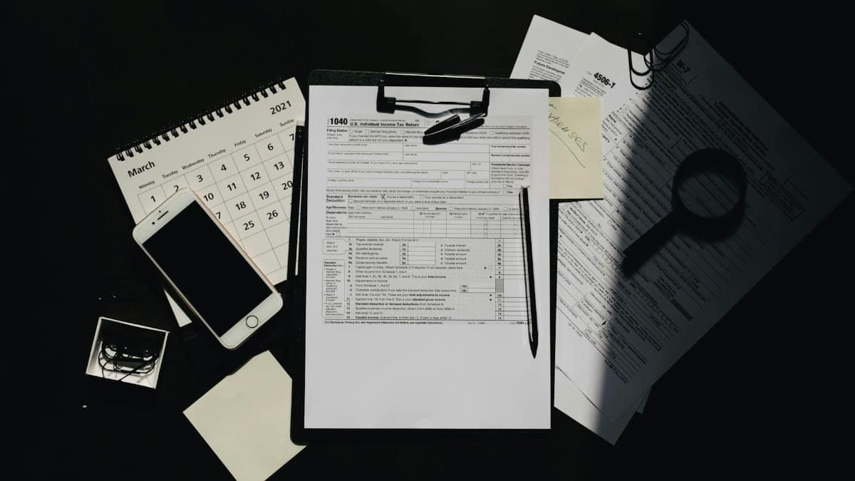 Flat lay of tax documents, calendar, and smartphone on a dark surface, symbolizing tax preparation.