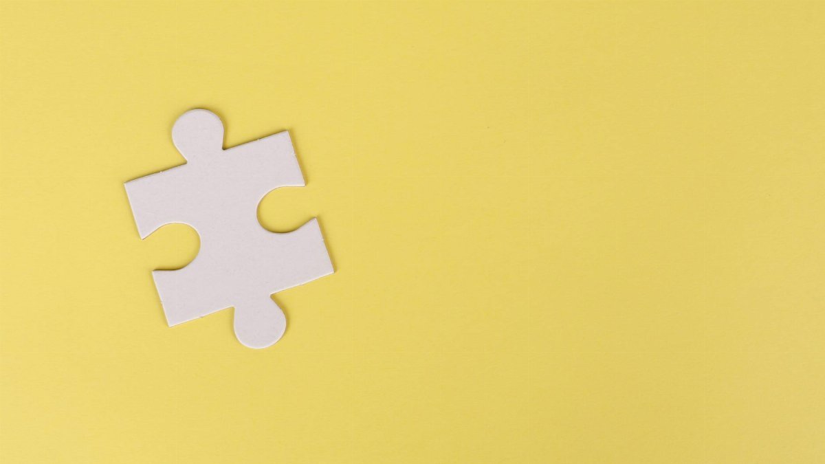 Simple white jigsaw puzzle piece placed on a bright yellow background with ample copy space.