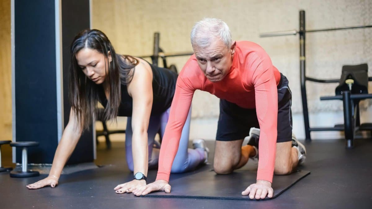 Senior man and female trainer performing fitness exercises indoors, promoting healthy aging.