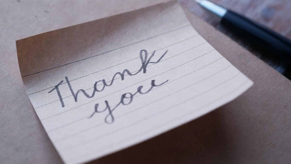 Close-up of a handwritten thank you note on brown paper with a pen nearby.