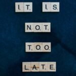 An inspiring message formed with wooden letter tiles on a dark surface: 'It is not too late'.