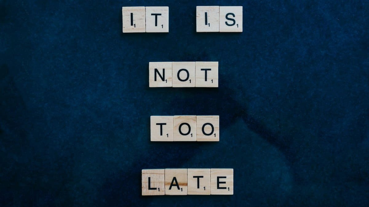 An inspiring message formed with wooden letter tiles on a dark surface: 'It is not too late'.