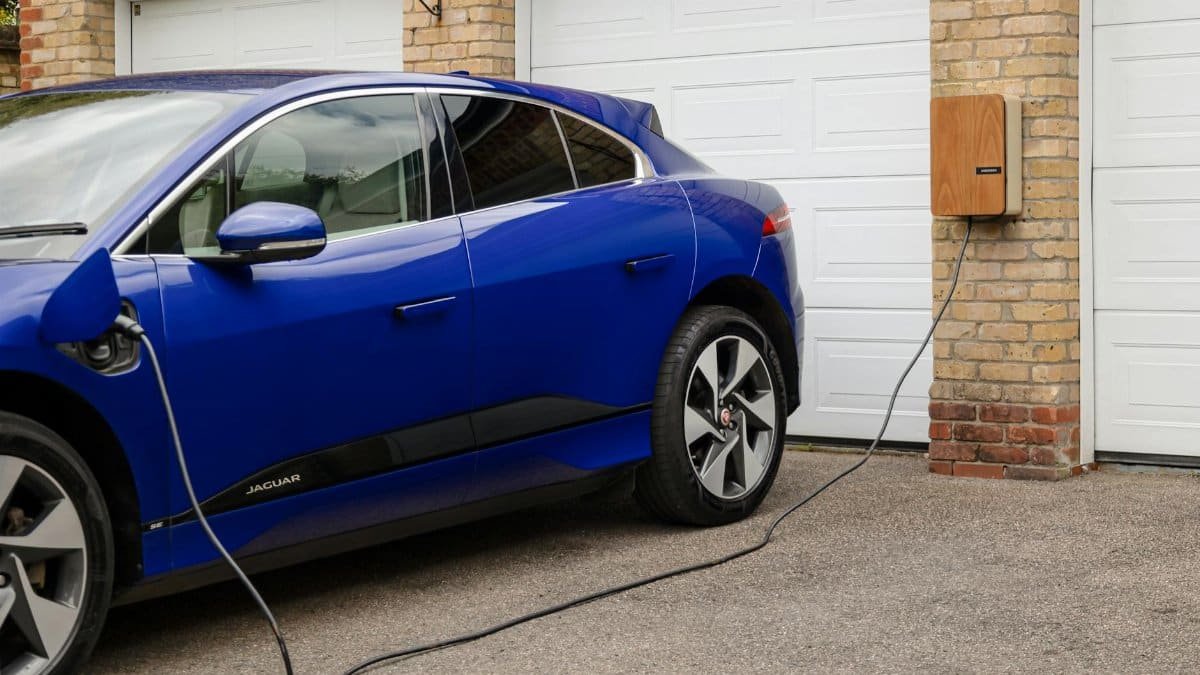 Blue electric vehicle charging at home using wall-mounted unit. Sustainable transportation solution.