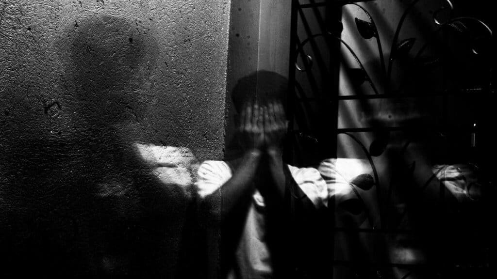 Grayscale image of a man covering his face, evoking themes of fear and introspection.