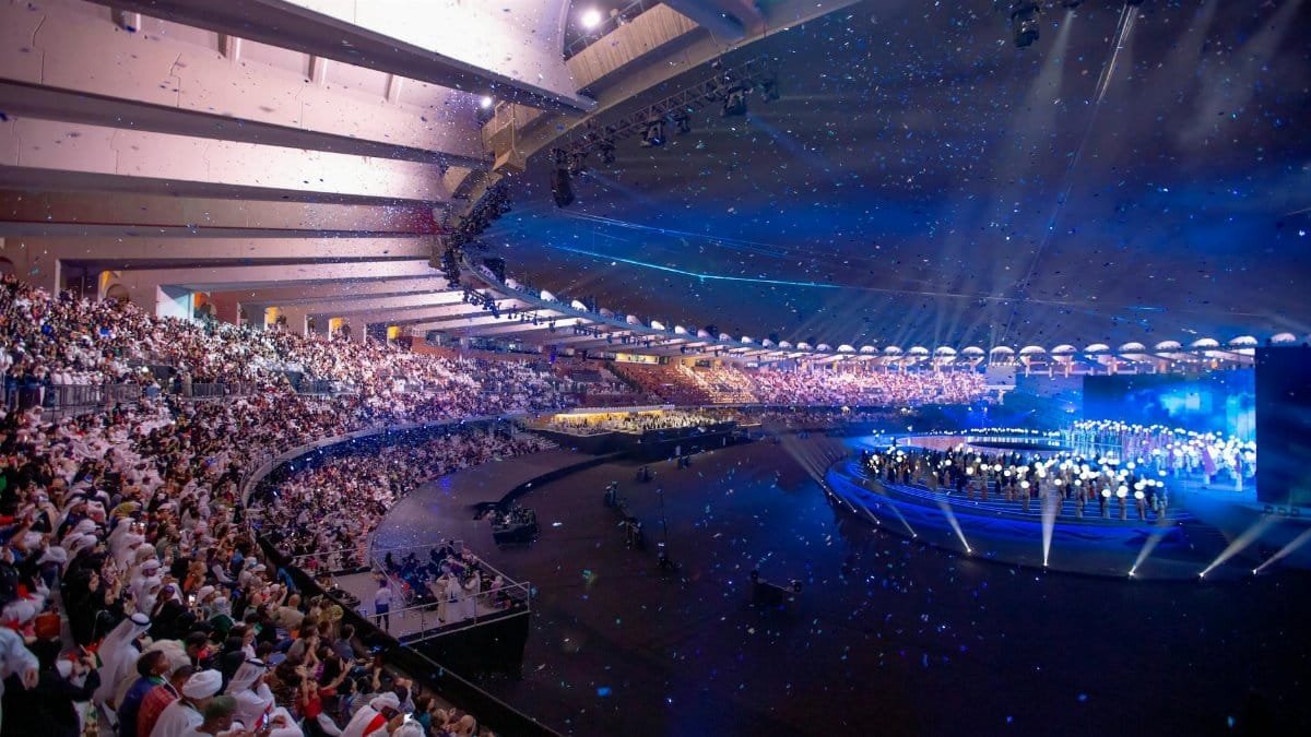 Massive arena concert with vibrant lights, packed audience, and dynamic stage performance.