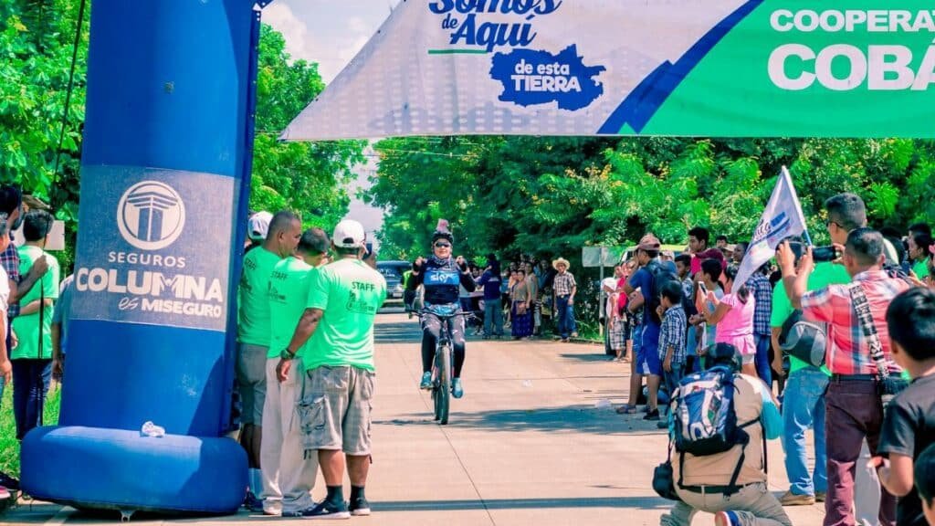 A cyclist reaches the finish line, cheered by a vibrant crowd at an outdoor race event.