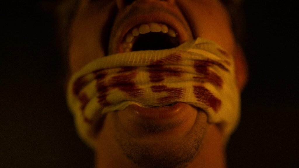 Close-up portrait of a screaming man with a blood-stained bandage covering his mouth, conveying pain and anguish.