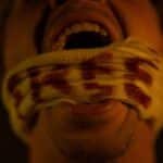 Close-up portrait of a screaming man with a blood-stained bandage covering his mouth, conveying pain and anguish.