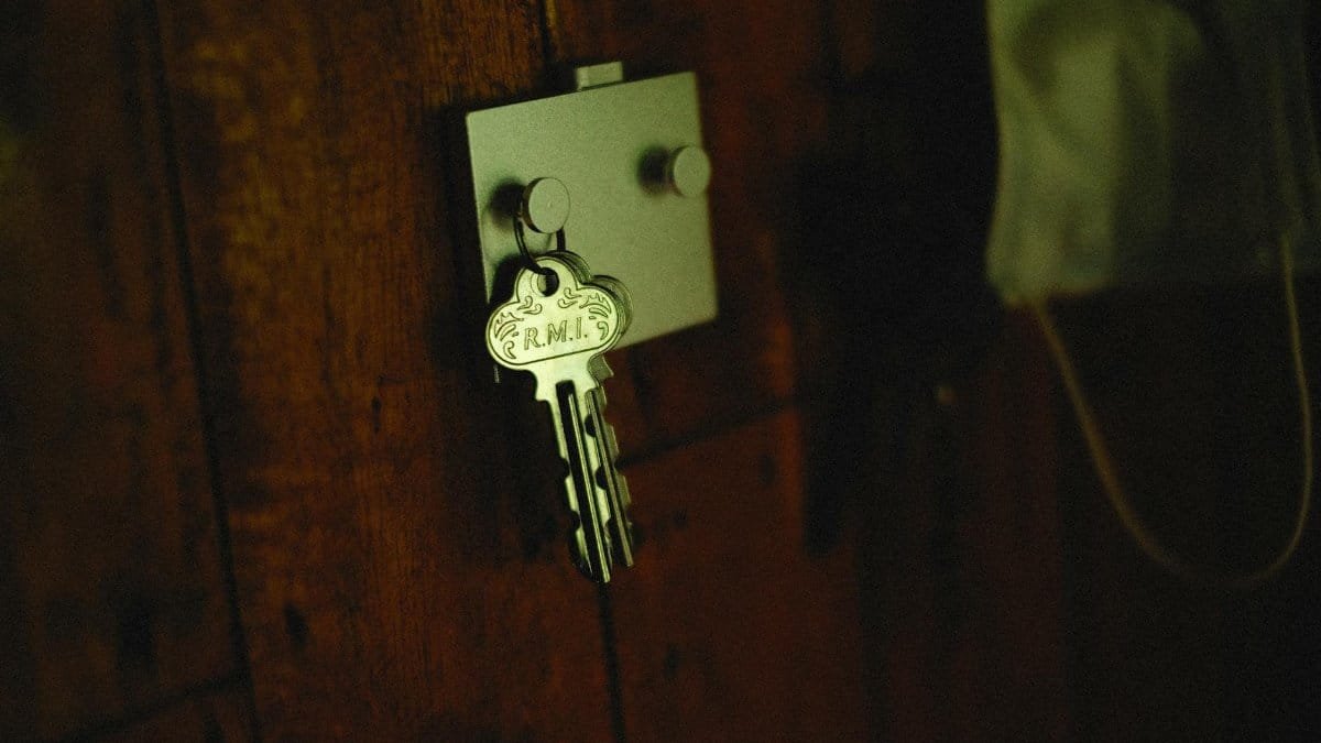 A close-up of a metallic key labeled 'R.M.I.' on a rustic wooden wall hook.