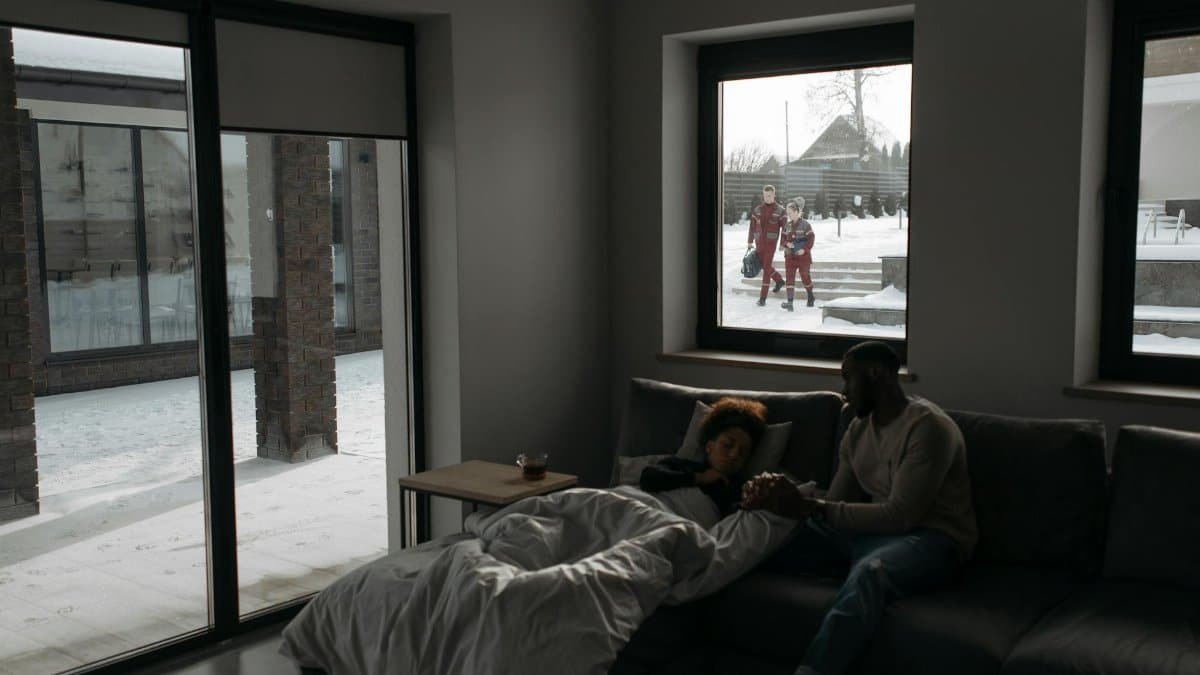 A couple indoors awaits paramedics for medical assistance, showing care and urgency.