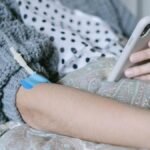 A woman receiving intravenous therapy for cancer treatment while using her phone, symbolizing connection and hope.
