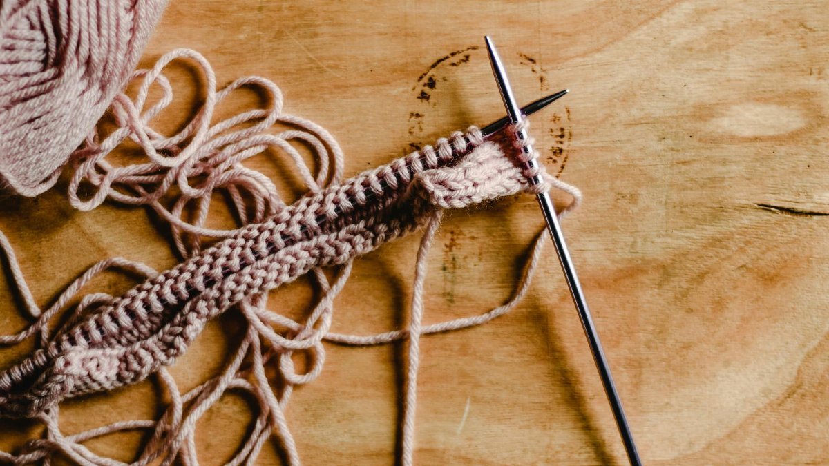 Detailed image of yarn and knitting needles on a wooden table with a close-focus on the crafting process.