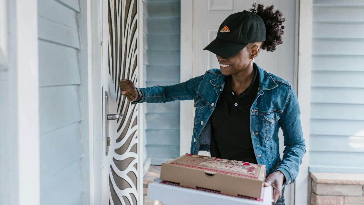 Smiling delivery woman knocking on front door holding pizza boxes.
