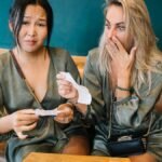 Two women express surprise while reviewing a restaurant bill in a casual setting.