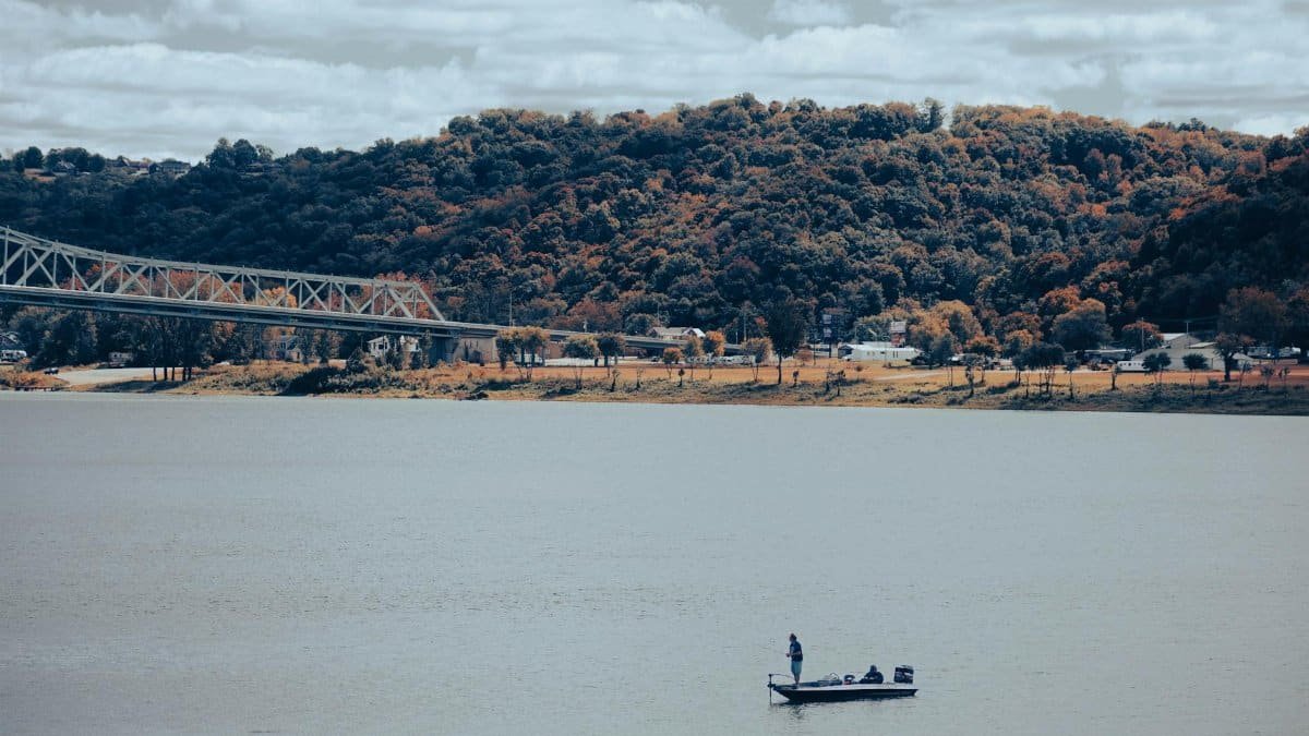 A tranquil scene featuring a boat on a lake with a bridge and forested hills in the background.