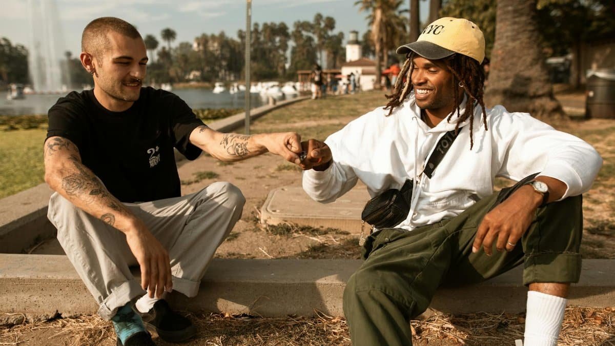 Two friends sitting outdoors in a park sharing a joyful fist bump, symbolizing friendship and support.