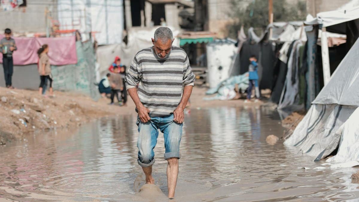 Middle-aged man in Gaza navigates flooded street with resilience, reflecting life challenges.