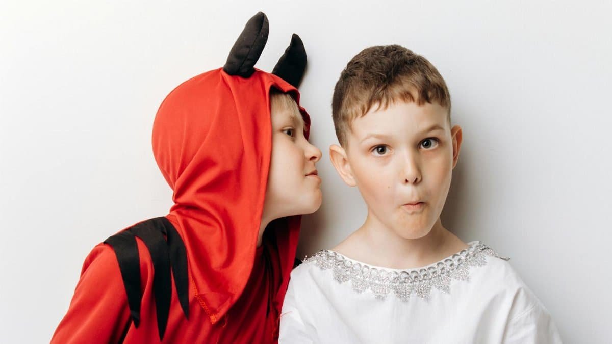 Two children dressed as an angel and a devil, displaying playful expressions against a white background.