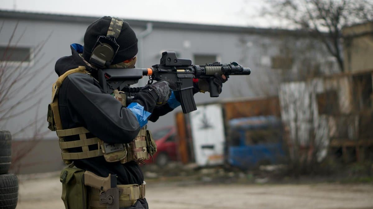 An airsoft player in full tactical gear aiming a rifle outdoors, showing action and focus.
