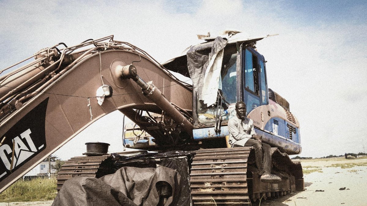 A man sits on an excavator under a blue sky in Lagos, Nigeria, capturing daily life.