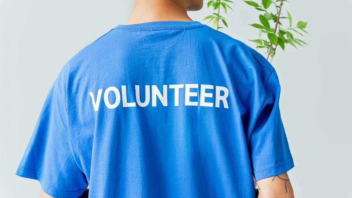 A person in a blue volunteer shirt stands in front of a plant.