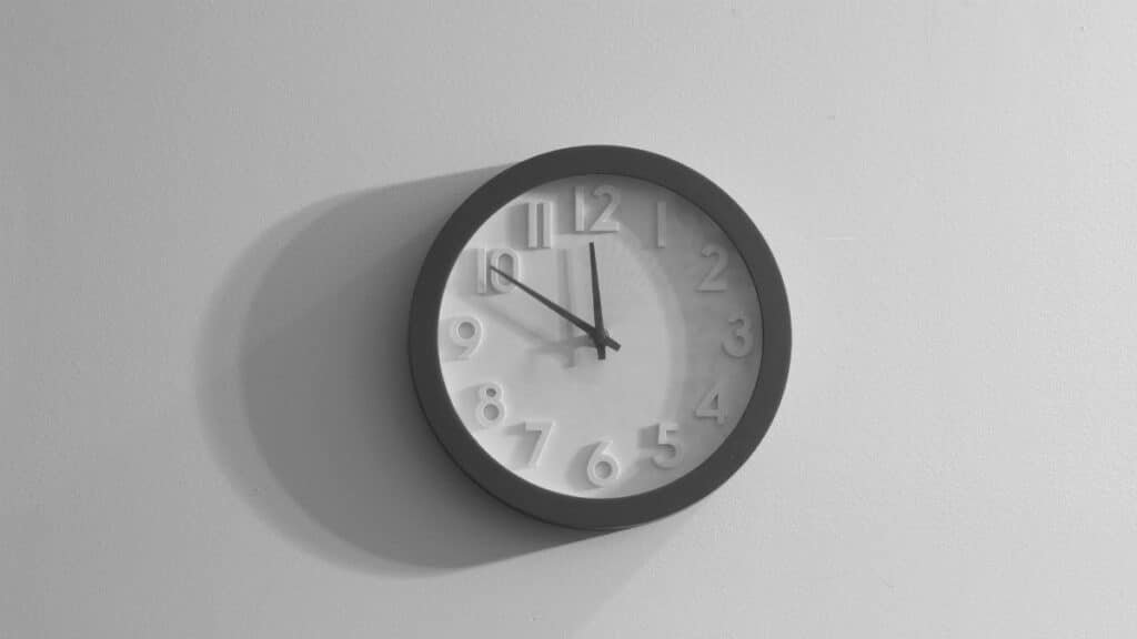 A black and white wall clock casting a shadow against a plain wall.