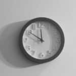 A black and white wall clock casting a shadow against a plain wall.