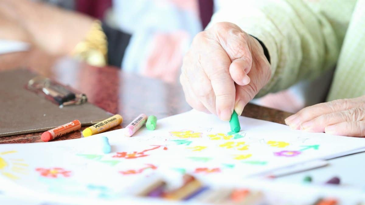 Close-up of a senior woman drawing with crayons in an art therapy session indoors.