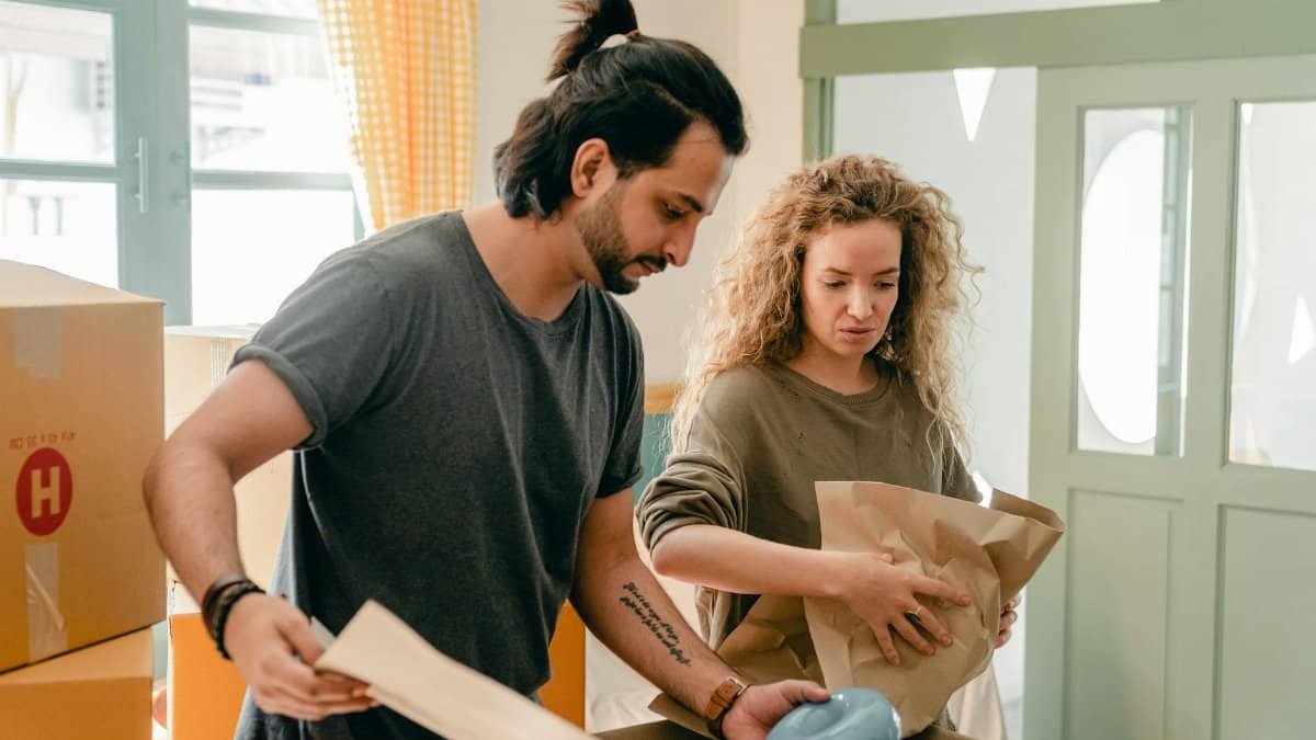 Concentrated young diverse couple using wrapping paper while packing belongings in carton boxes during relocation