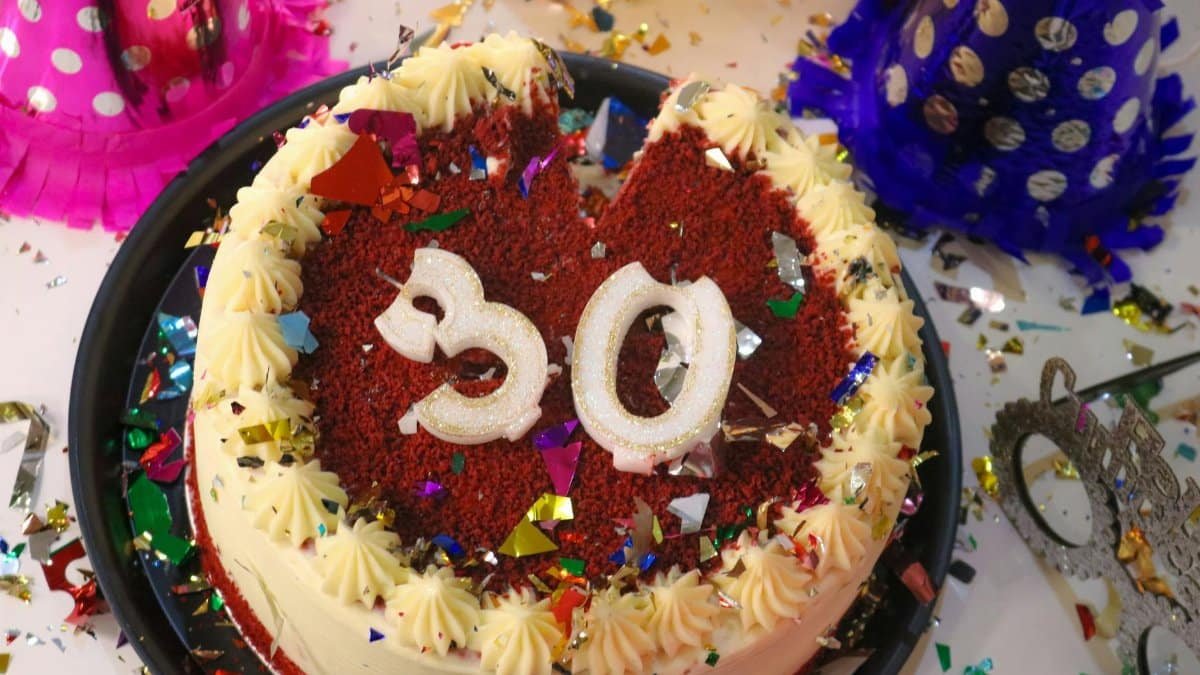 Vibrant red velvet cake with number 30 decoration, surrounded by confetti and party hats.