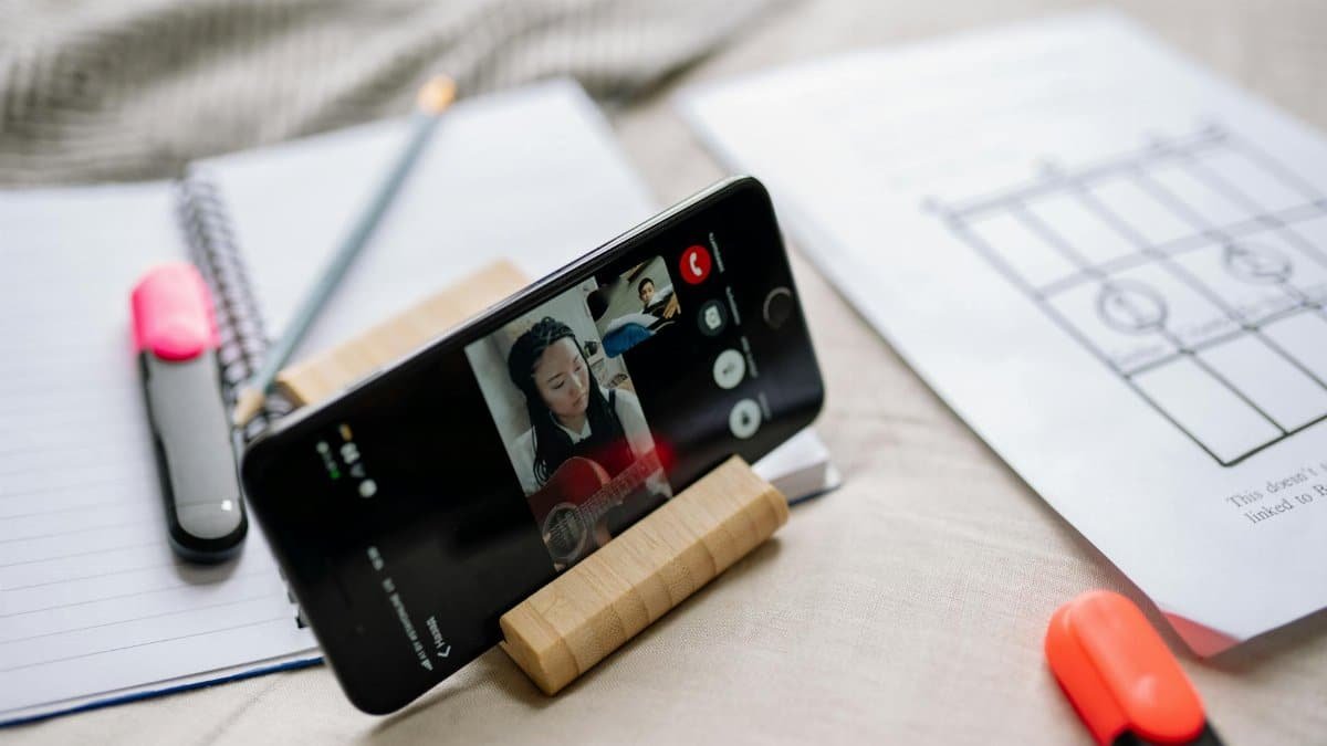 A smartphone on a stand shows a virtual guitar lesson with sheets and highlighters nearby, illustrating online learning.